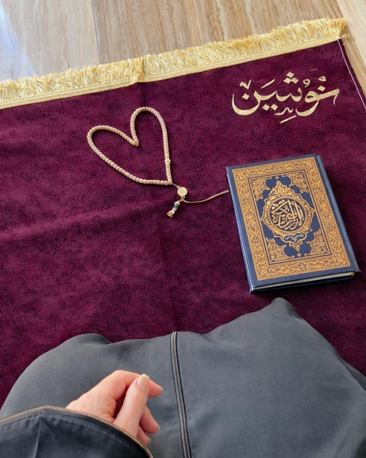 Purple prayer rug with a Quran and rosary on a wooden floor
